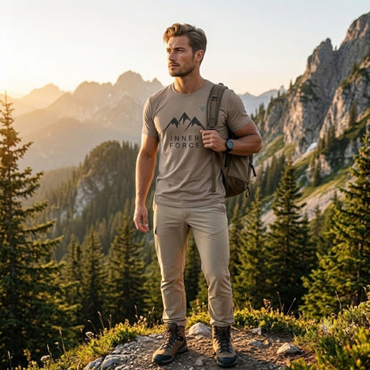 Man wearing the HorizonVibe Inner Force Trail Tee Hiking Edition while standing on a mountain trail with a hiking backpack, outdoor adventure scenery and alpine peaks at golden hour.